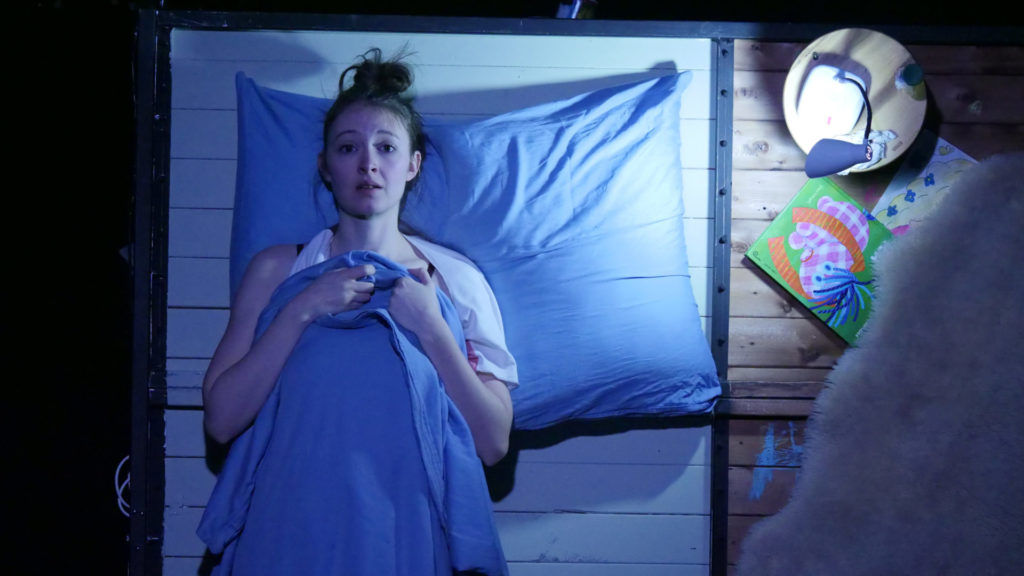 © Foto: Richard Schmetterer Frau liegt in angedeutetem Bett und blickt ängstlich nach vorne.