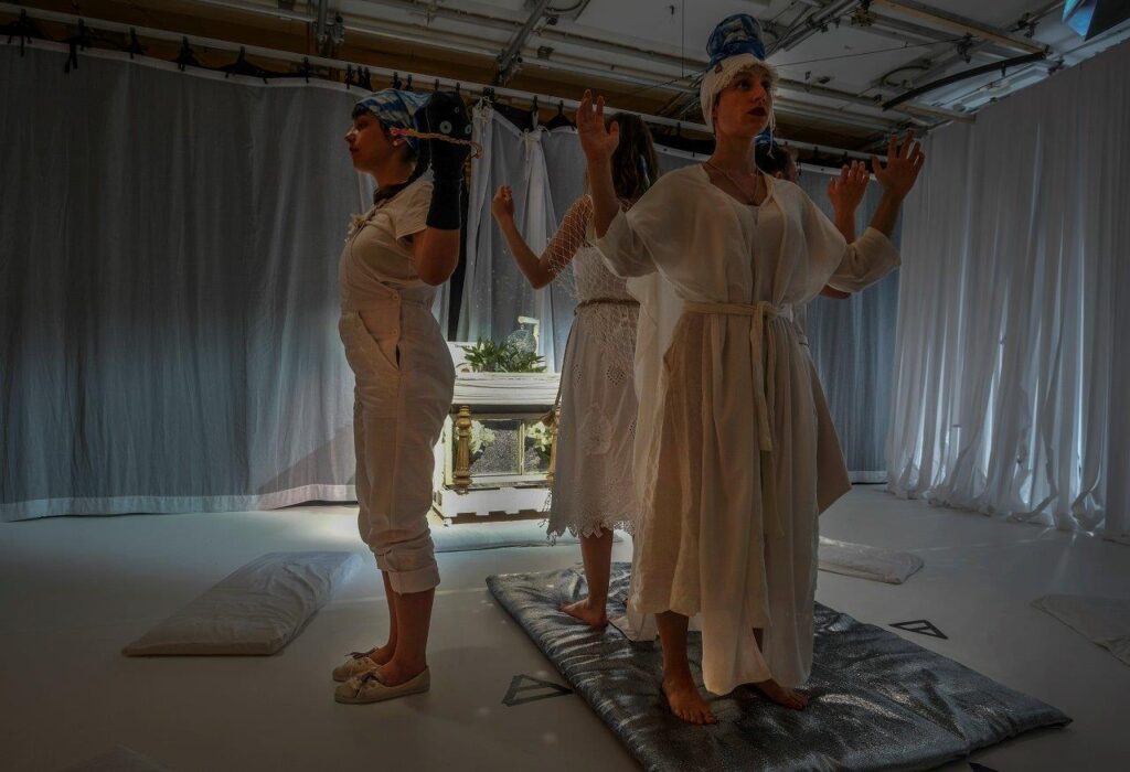 © Foto: Rainer Berson Vier Gestalten in weißen Gewändern stehen mit dem Rücken zueinander und reichen sich die Hände