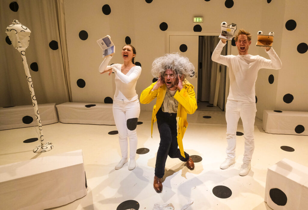 © Foto: Rainer Berson Mann in gelbem Regenmantel, umgeben von zwei Klappmaulpuppen, schreit,